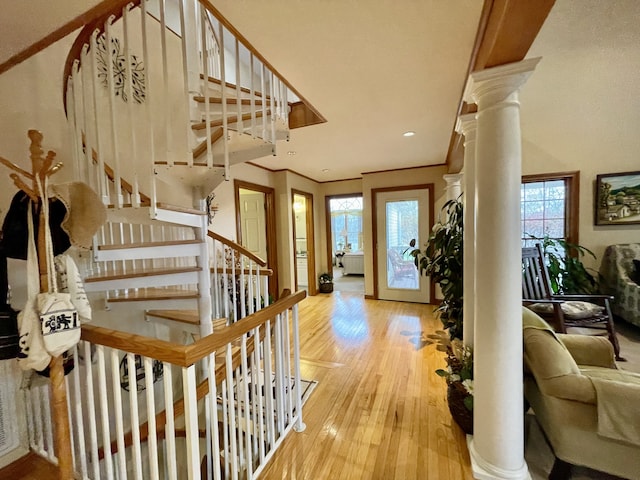 entryway with light wood-type flooring, decorative columns, and crown molding