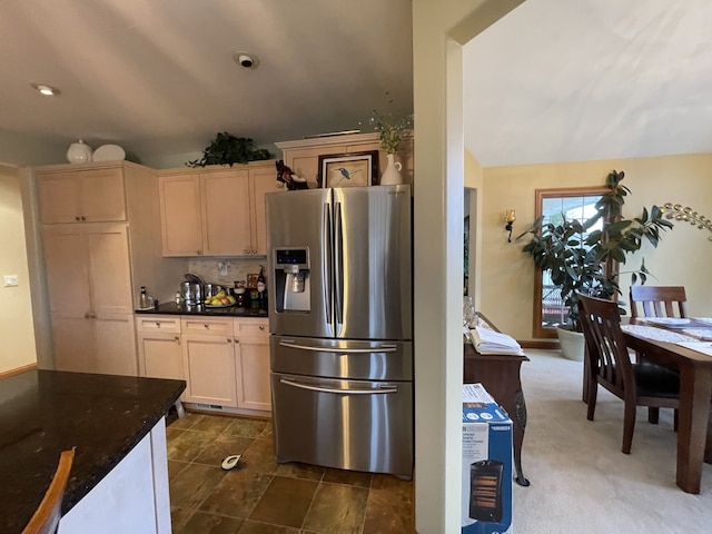 kitchen with light brown cabinets, dark colored carpet, dark stone countertops, stainless steel fridge, and decorative backsplash