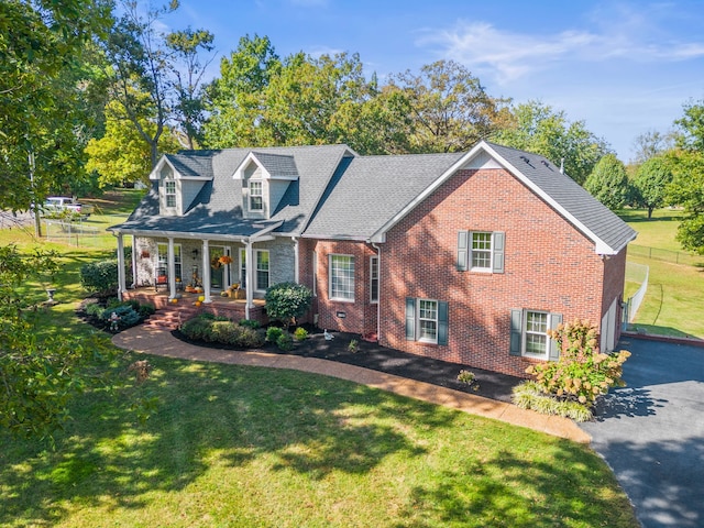 cape cod home featuring covered porch, brick siding, aphalt driveway, and a front yard