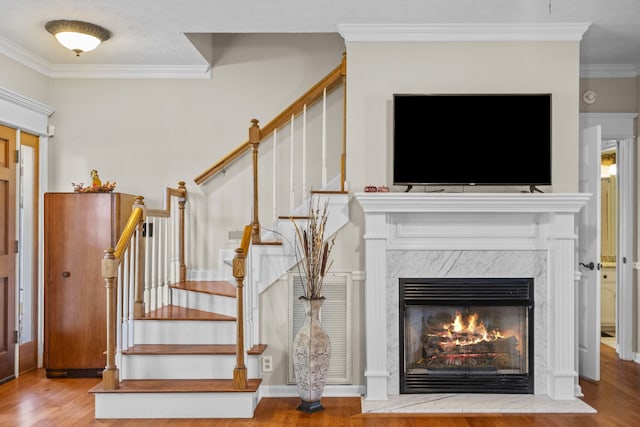 unfurnished living room with stairs, ornamental molding, a premium fireplace, and wood finished floors