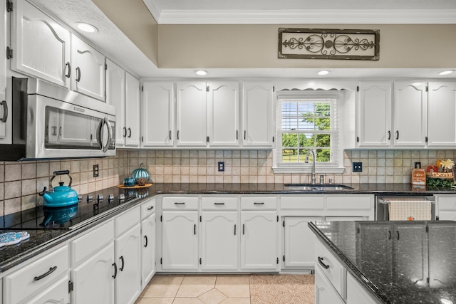 kitchen with light tile patterned floors, stainless steel appliances, a sink, ornamental molding, and dark stone countertops