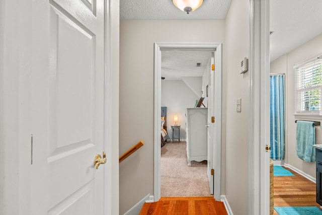 hallway featuring an upstairs landing, baseboards, a textured ceiling, and wood finished floors