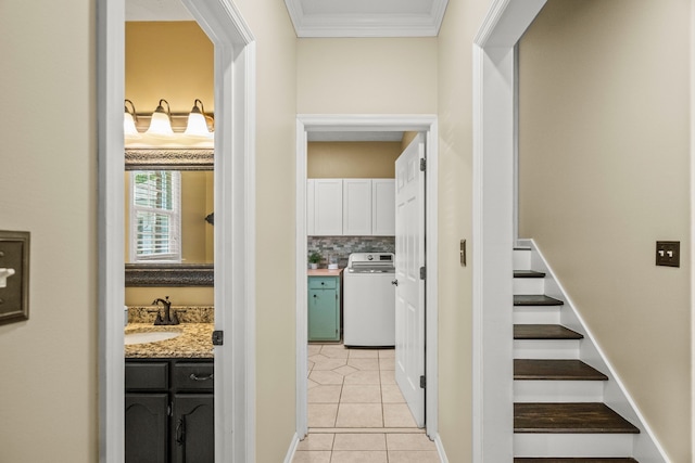 hallway featuring washer / dryer, light tile patterned floors, ornamental molding, and a sink