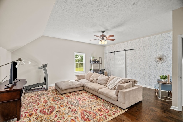 living room with a textured ceiling, vaulted ceiling, ceiling fan, a barn door, and dark hardwood / wood-style floors