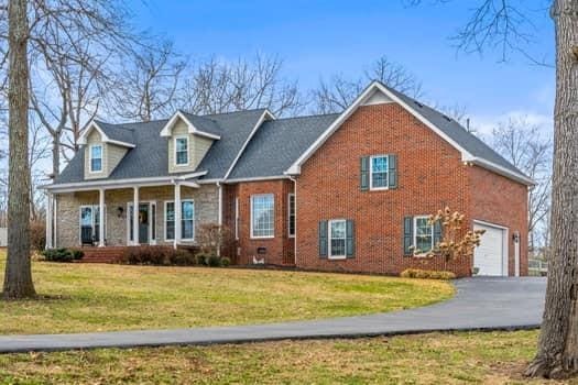 view of front facade with driveway, covered porch, a front lawn, and brick siding