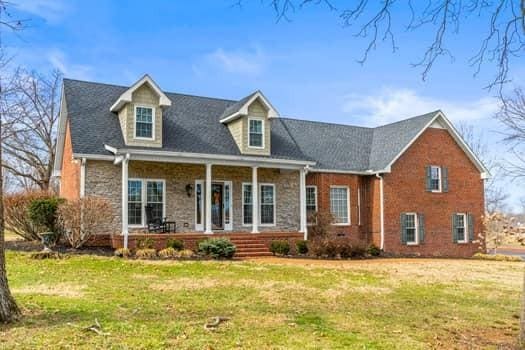 cape cod house with covered porch, stone siding, and a front lawn