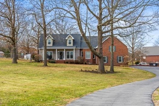 cape cod home with driveway, a porch, and a front yard