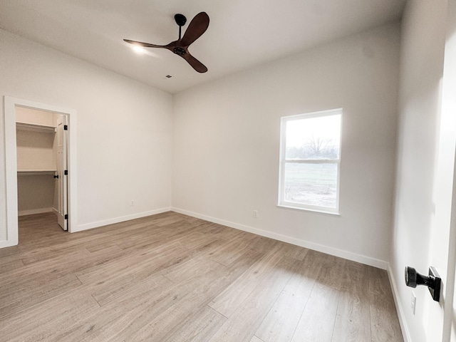 unfurnished bedroom featuring light wood finished floors, a walk in closet, a ceiling fan, and baseboards