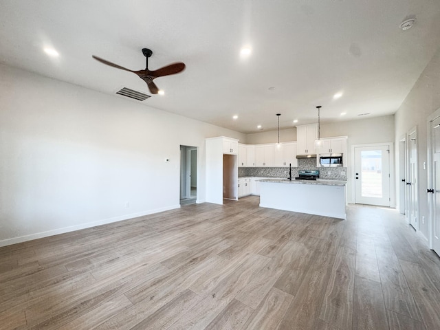 unfurnished living room featuring a ceiling fan, light wood-type flooring, visible vents, and baseboards