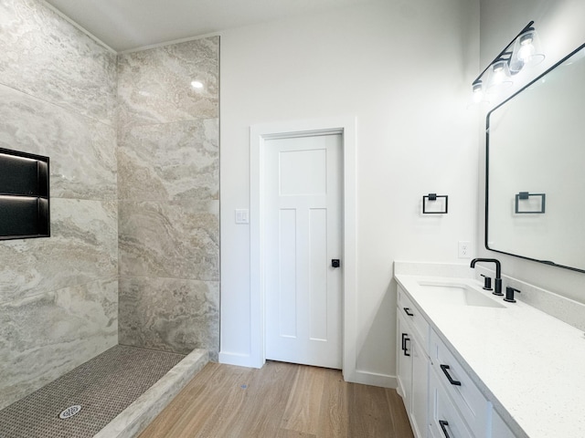 full bathroom with a tile shower, wood finished floors, vanity, and baseboards