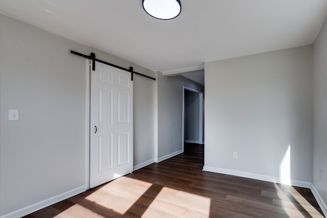 unfurnished bedroom with a barn door and dark hardwood / wood-style floors