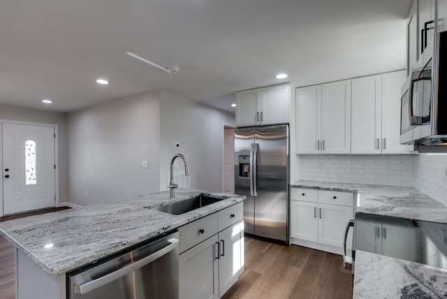 kitchen with a center island with sink, sink, appliances with stainless steel finishes, light stone counters, and white cabinetry