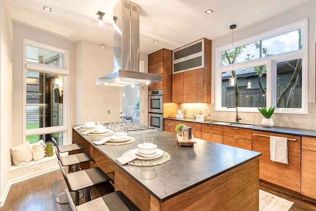 kitchen featuring island range hood, a breakfast bar area, hanging light fixtures, and dark wood-type flooring