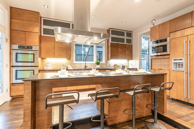 kitchen with a center island, island range hood, dark hardwood / wood-style flooring, and double oven