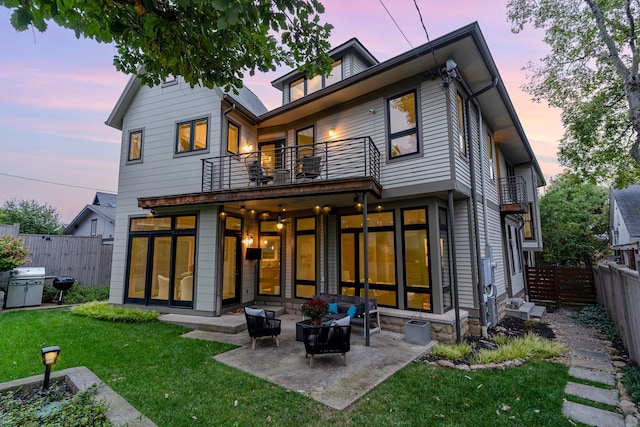 back house at dusk with a yard, an outdoor hangout area, a balcony, and a patio area