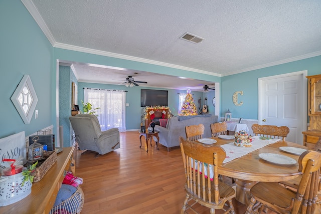 dining space featuring ceiling fan, ornamental molding, a textured ceiling, and light wood-type flooring