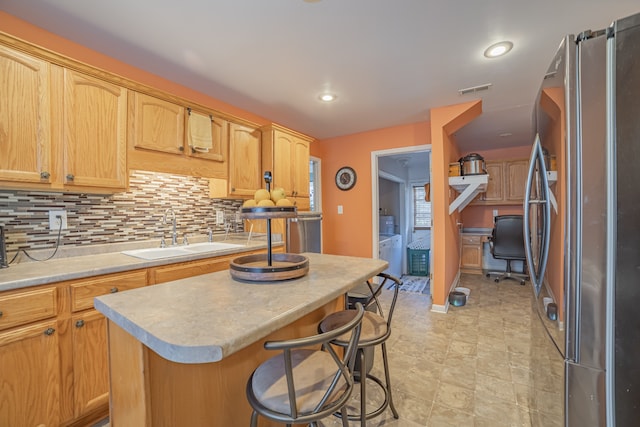 kitchen featuring tasteful backsplash, washing machine and dryer, sink, a center island, and stainless steel refrigerator