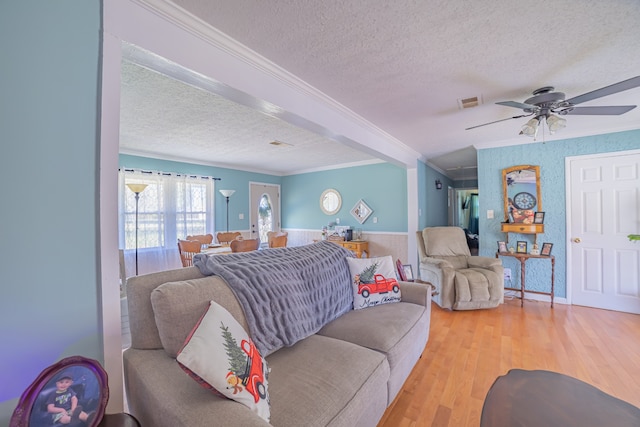 living room with a textured ceiling, light wood-type flooring, ceiling fan, and ornamental molding