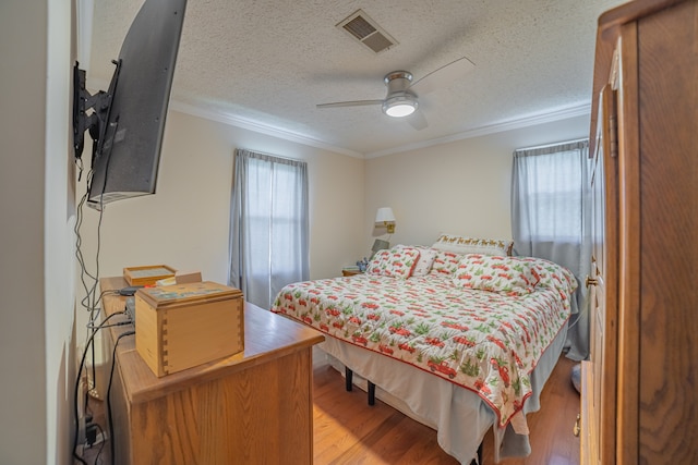 bedroom with a textured ceiling, ceiling fan, light wood-type flooring, and ornamental molding