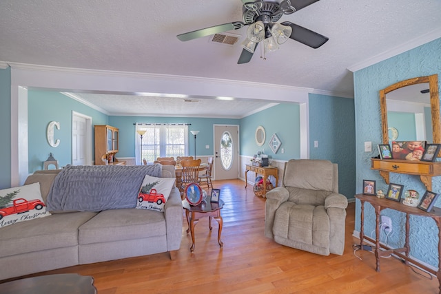 living room featuring ceiling fan, ornamental molding, a textured ceiling, and light hardwood / wood-style flooring