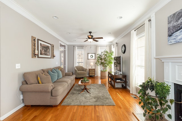 living room featuring ceiling fan, a healthy amount of sunlight, wood-type flooring, and ornamental molding