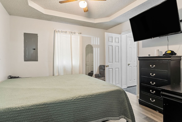 bedroom featuring ceiling fan, a raised ceiling, electric panel, a textured ceiling, and hardwood / wood-style flooring