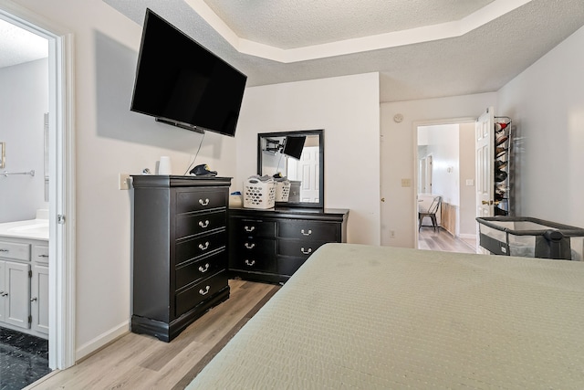 bedroom with a tray ceiling, ensuite bath, light hardwood / wood-style floors, and a textured ceiling