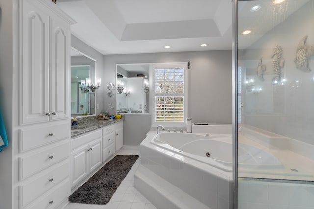 bathroom with a raised ceiling, vanity, tiled bath, and tile patterned floors