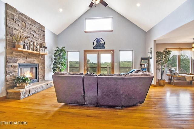 living room featuring a stone fireplace, ceiling fan, high vaulted ceiling, and wood-type flooring