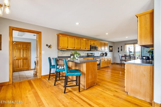 kitchen with a breakfast bar, light hardwood / wood-style flooring, decorative backsplash, kitchen peninsula, and stainless steel appliances