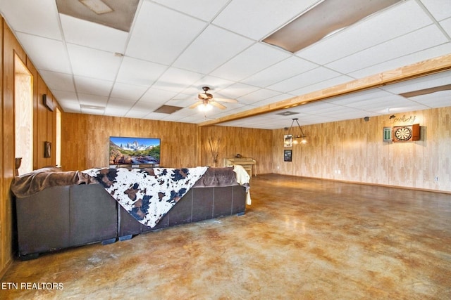 living room with ceiling fan, wood walls, and a drop ceiling