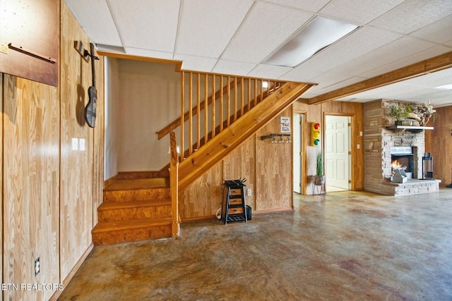 basement featuring a paneled ceiling, a stone fireplace, and wooden walls