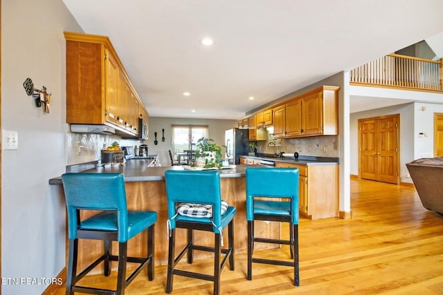 kitchen featuring stainless steel refrigerator, tasteful backsplash, a kitchen breakfast bar, light hardwood / wood-style flooring, and kitchen peninsula