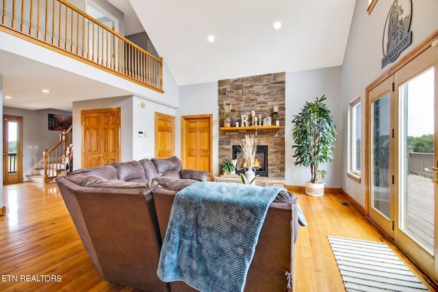 living room with a stone fireplace, high vaulted ceiling, a healthy amount of sunlight, and light wood-type flooring