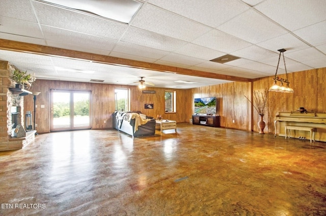 unfurnished living room featuring wood walls, a drop ceiling, ceiling fan, and concrete floors