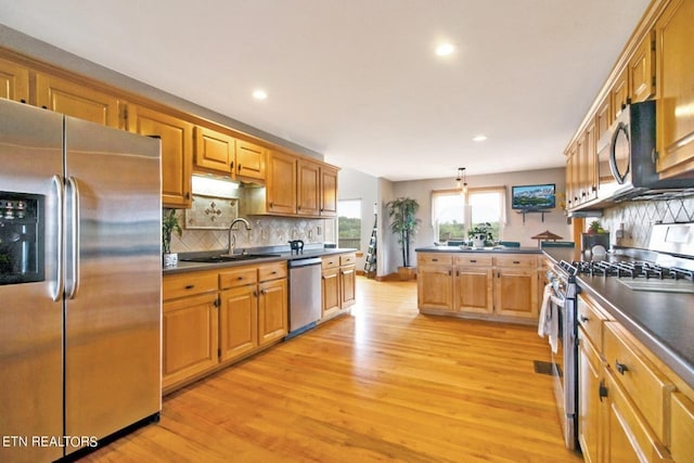 kitchen featuring sink, light hardwood / wood-style flooring, pendant lighting, decorative backsplash, and appliances with stainless steel finishes