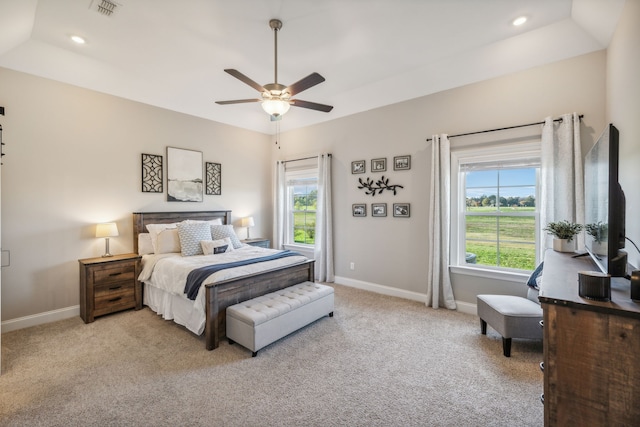 carpeted bedroom featuring ceiling fan, a raised ceiling, and multiple windows