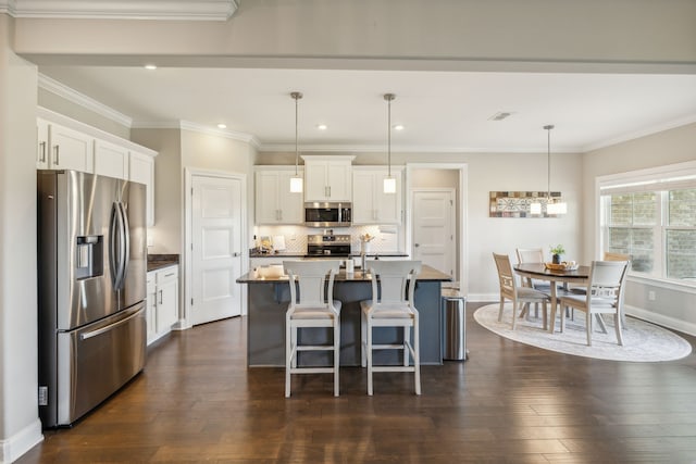 kitchen featuring appliances with stainless steel finishes, dark hardwood / wood-style flooring, a kitchen island with sink, decorative light fixtures, and white cabinetry