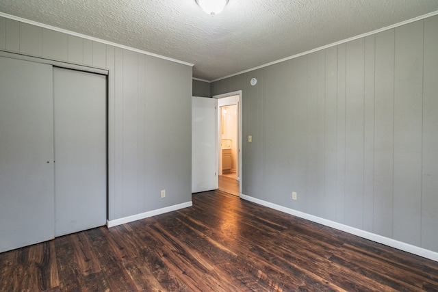 unfurnished bedroom with wood walls, crown molding, dark wood-type flooring, and a closet