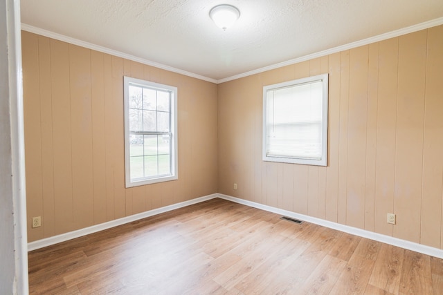 empty room featuring light hardwood / wood-style flooring, ornamental molding, and wood walls