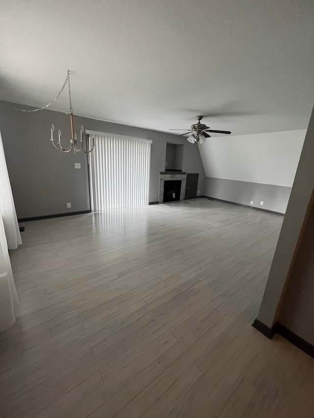 unfurnished living room with hardwood / wood-style floors, ceiling fan with notable chandelier, lofted ceiling, and a tile fireplace