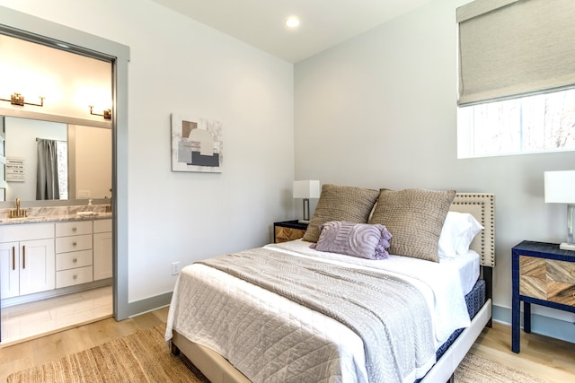 bedroom featuring sink, light wood-type flooring, ensuite bathroom, and multiple windows