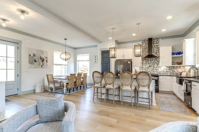 kitchen featuring appliances with stainless steel finishes, light hardwood / wood-style floors, pendant lighting, wall chimney exhaust hood, and white cabinets