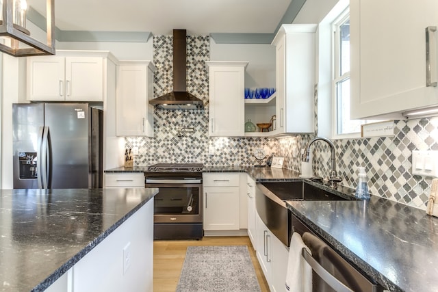 kitchen with stainless steel appliances, wall chimney range hood, light wood-type flooring, and white cabinetry