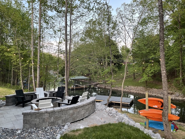 view of patio with a boat dock, a fire pit, and a water view