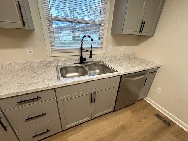 kitchen with dishwasher, sink, gray cabinets, light hardwood / wood-style floors, and light stone counters