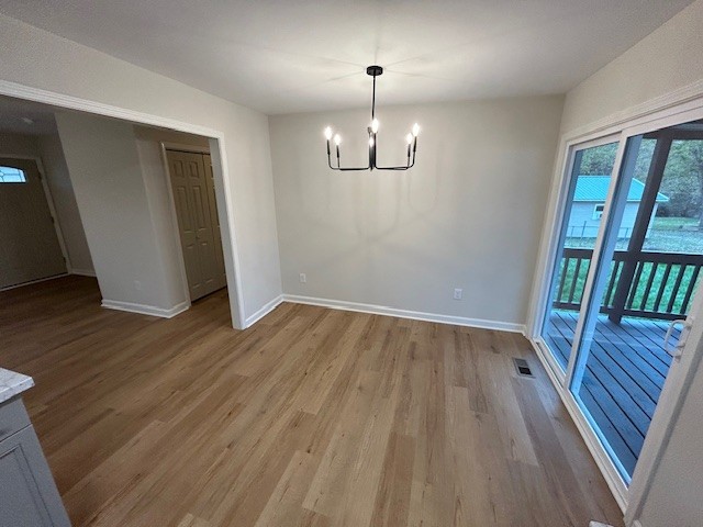 unfurnished dining area with a notable chandelier and light wood-type flooring