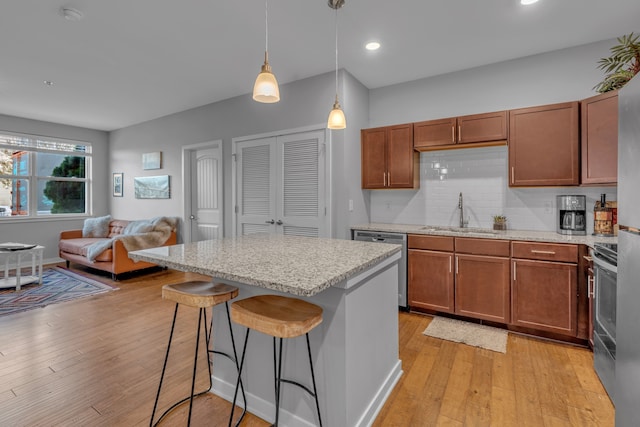 kitchen featuring sink, stainless steel appliances, light hardwood / wood-style floors, decorative light fixtures, and a breakfast bar