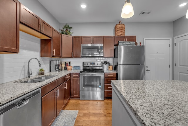 kitchen featuring hanging light fixtures, sink, light stone countertops, appliances with stainless steel finishes, and light hardwood / wood-style floors