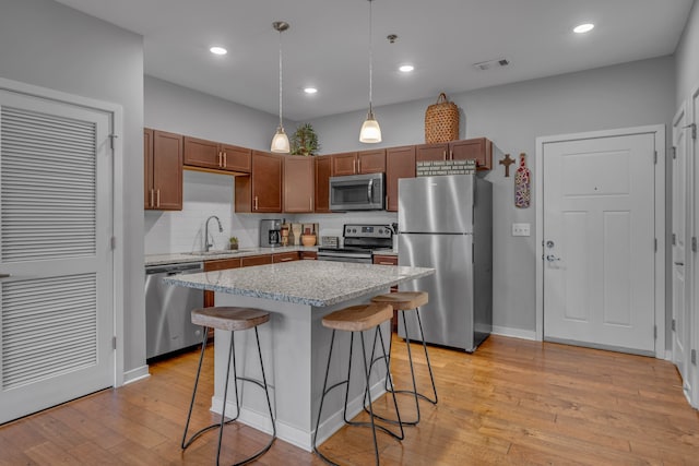 kitchen with hanging light fixtures, a kitchen island, light hardwood / wood-style floors, a kitchen bar, and stainless steel appliances